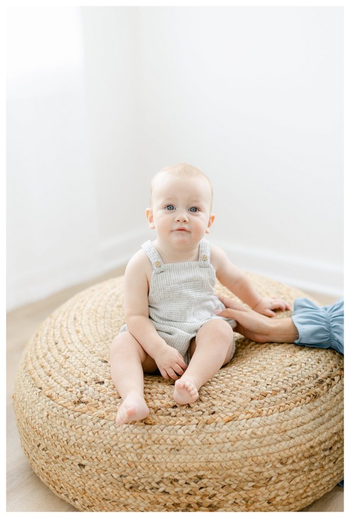 9 month old infant sitting on a rattan pouf photographed by Tara Federico
