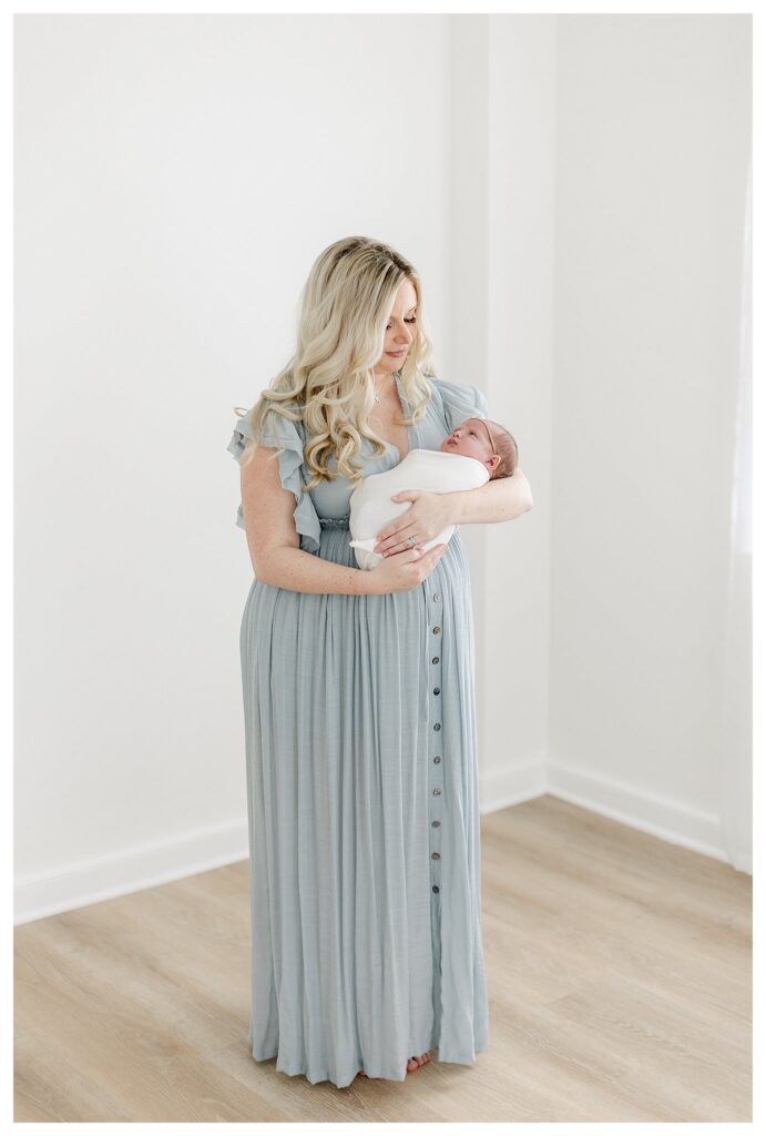 Mom wearing dusty blue dress holding her newborn baby girl photographed by Philadelphia Newborn Photographer Tara Federico