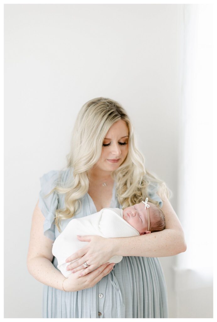 Beautiful blonde mom holding her babygirl in a natural light studio captured by Philadelphia Newborn Photographer Tara Federico