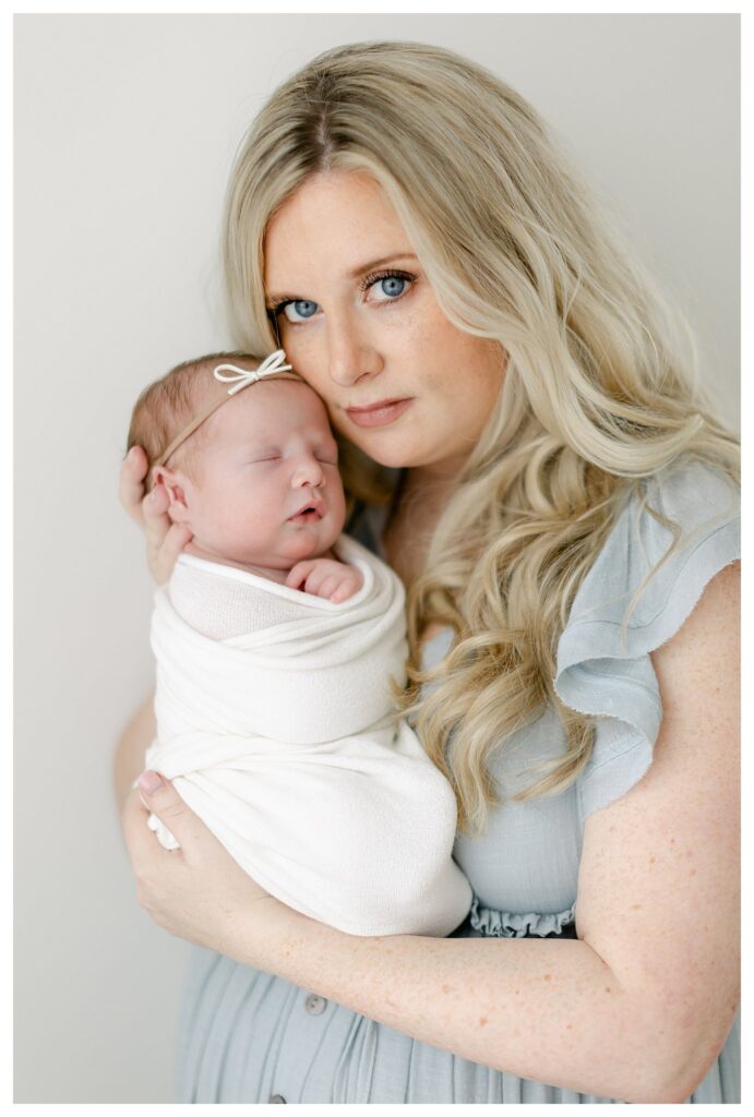 Close up shot of Beautiful blonde mom holding her babygirl in a natural light studio captured by Philadelphia Newborn Photographer Tara Federico