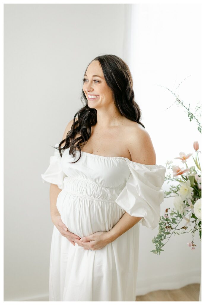 Beautiful expectant mom wearing a white dress surrounded by blush florals for her maternity session in Charleston by Tara Federico photography