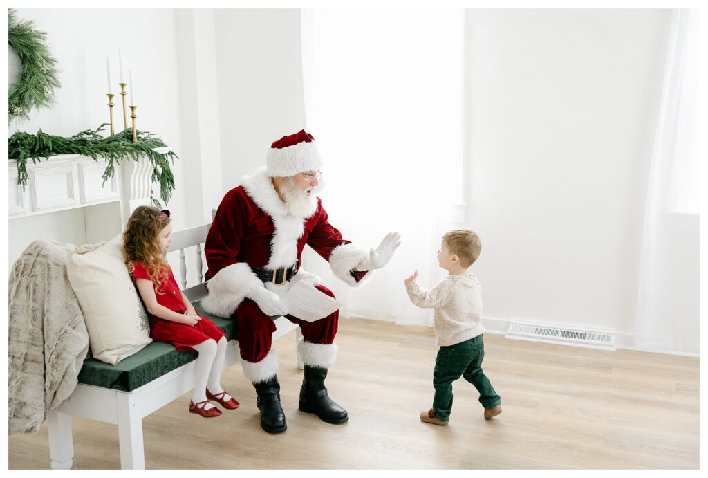 Little boy giving Santa a high five during his photoshoot in Tara Federico Photography's brightly lit studio