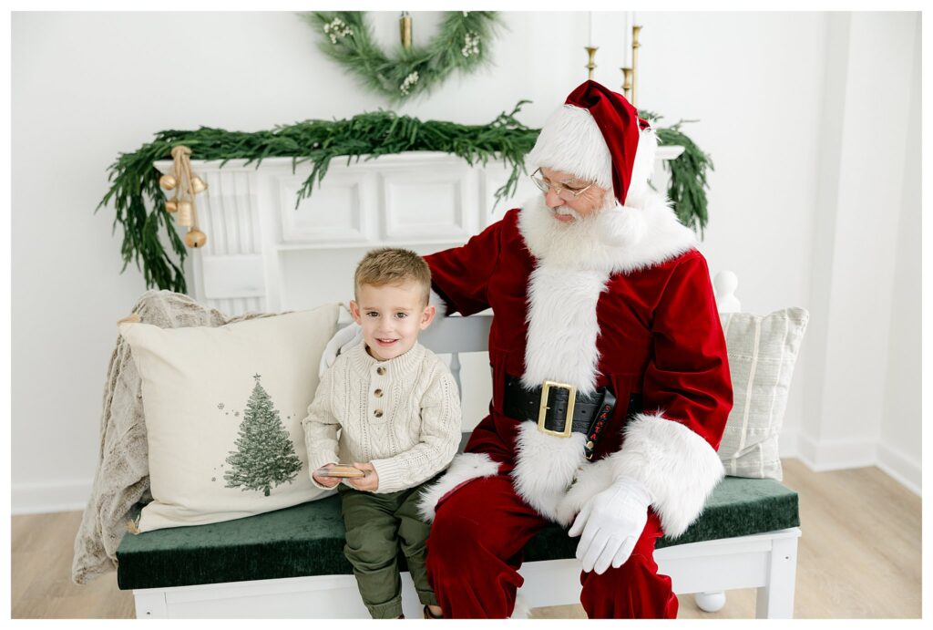 Little boy sitting next to Santa holding a cookie during his South Jersey Santa Pictures