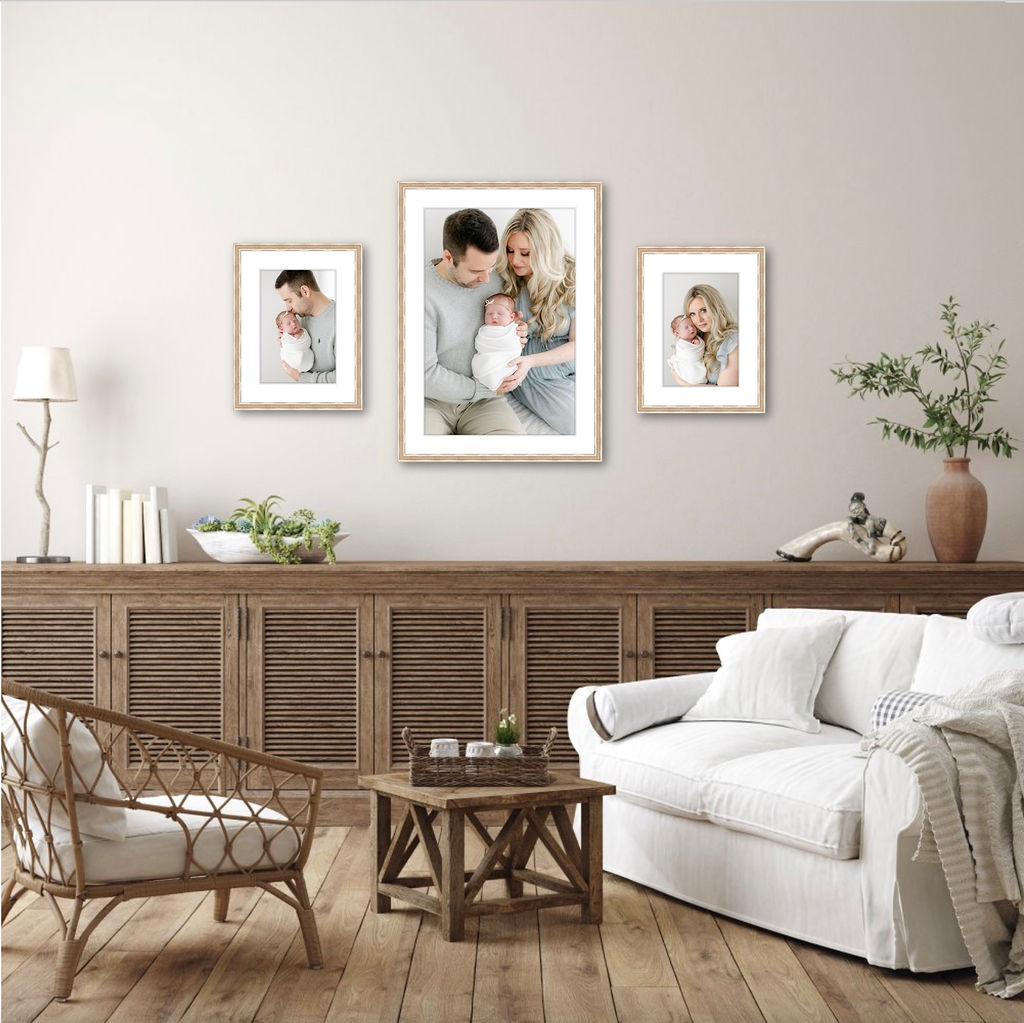 Framed newborn photos hang on a wall in a living room