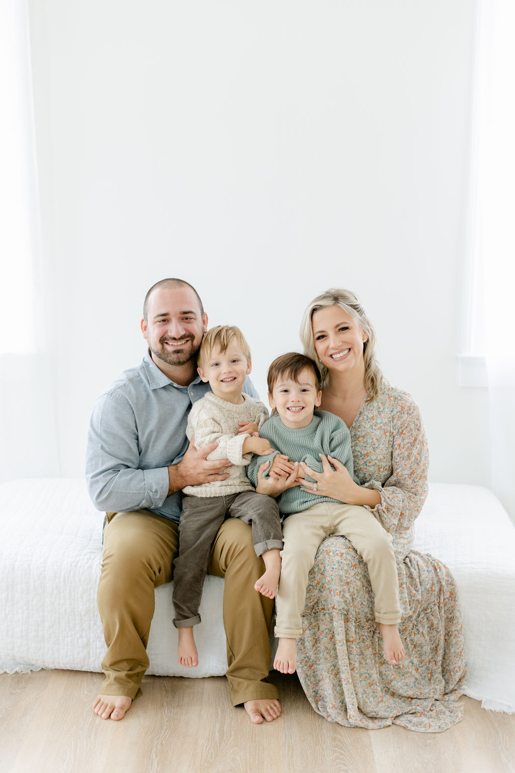 A mom and dad sit on the edge of a bed in a studio holding their two toddler sons in their laps before visiting family friendly restaurants charleston sc