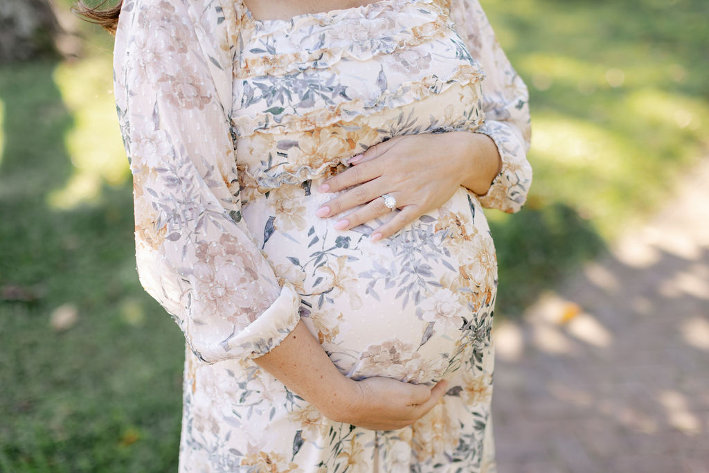 Details of a mother to be holding her bump in a floral print maternity dress