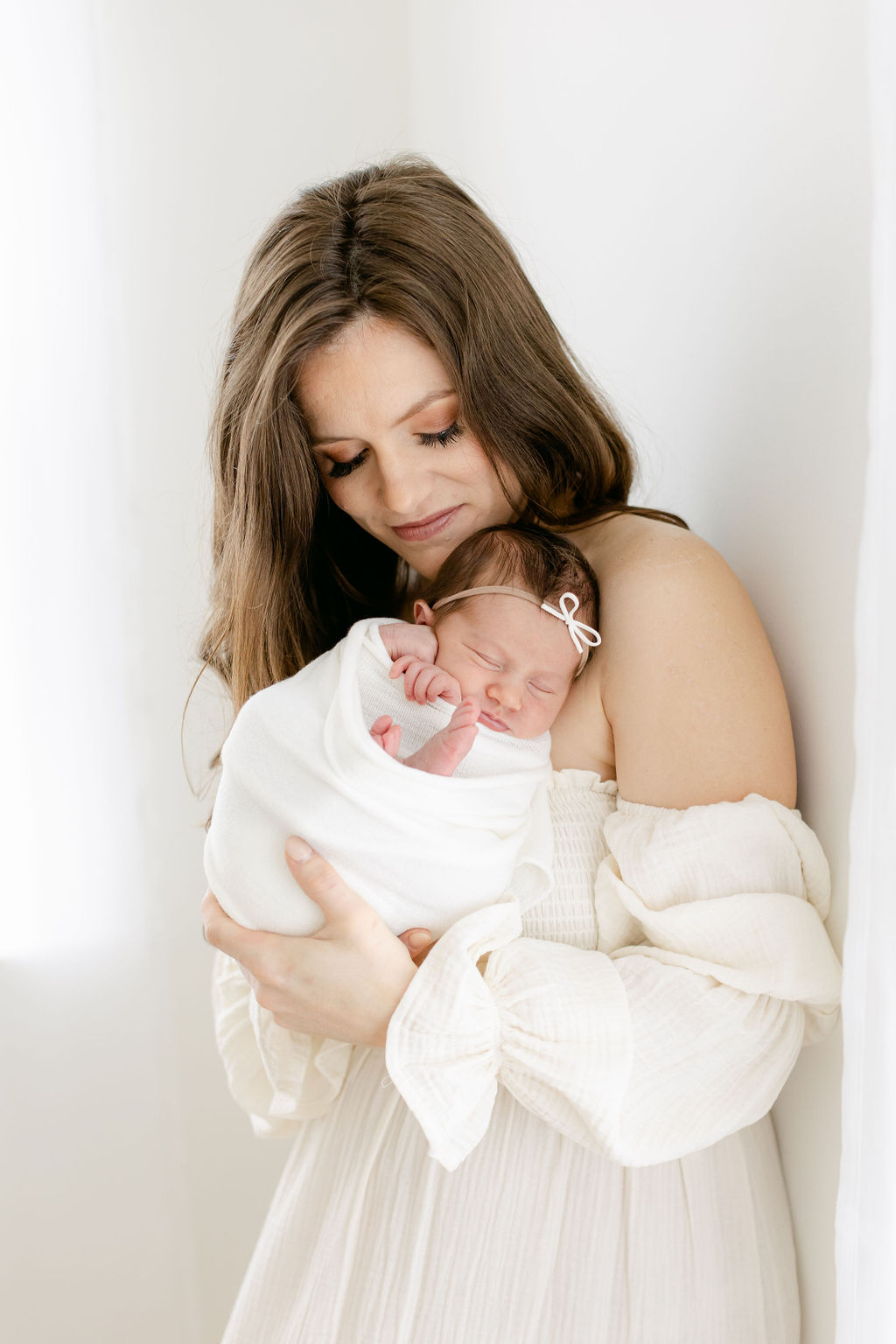 A happy mother cradles her sleeping newborn baby against her chest while leaning against a wall in a studio before meeting pediatricians mount pleasant sc