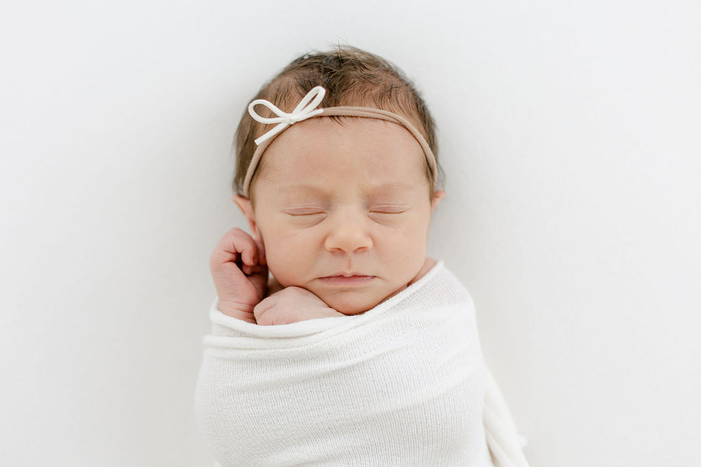 A newborn baby girl sleeps in a white swaddle and small bow before meeting pediatricians mount pleasant sc