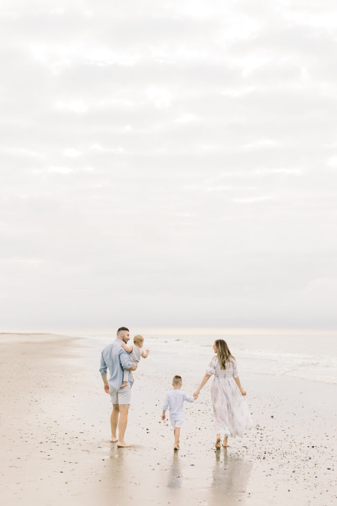 Parents holding hands with their two young sons, walking along the shoreline of Isle of Palms