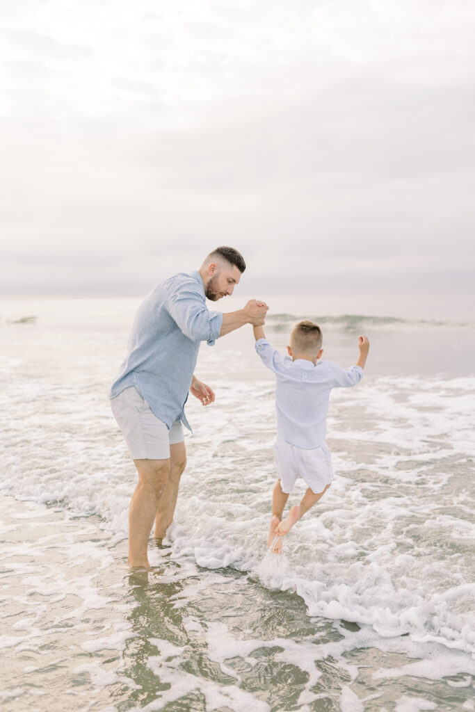 Father holding his oldest son's hand, jumping the waves of Isle of Palms