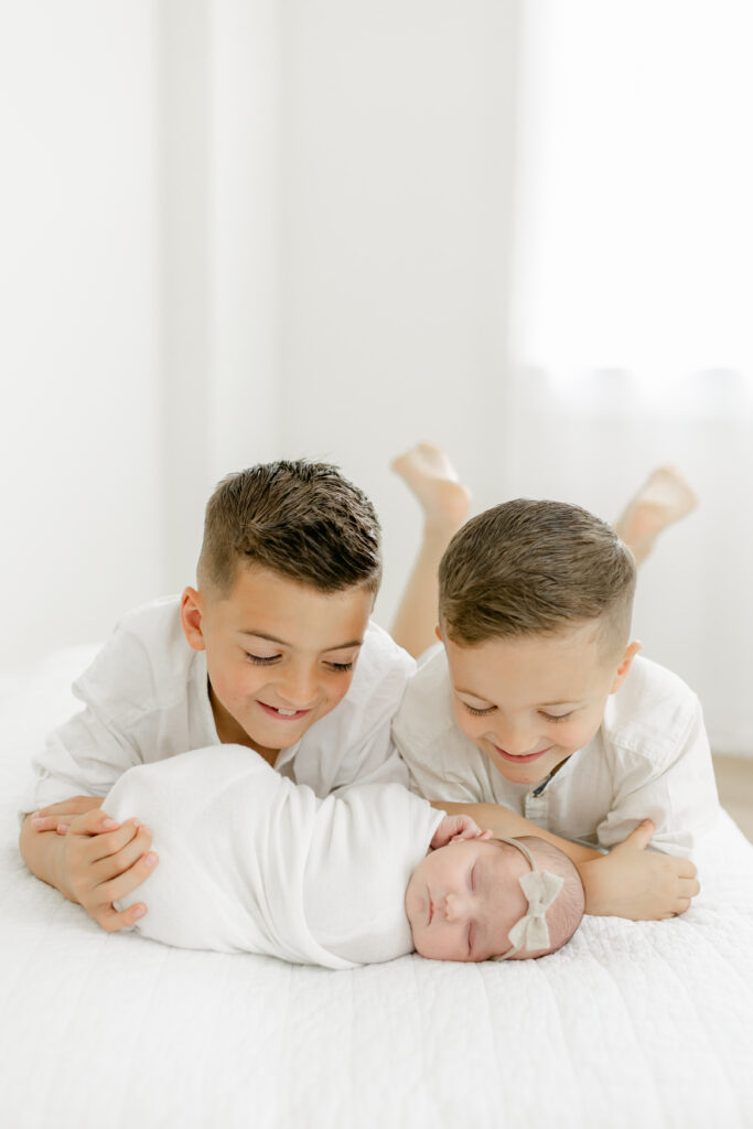 Heartwarming moment as two brothers proudly hold their newborn sister during a Charleston newborn photography session.