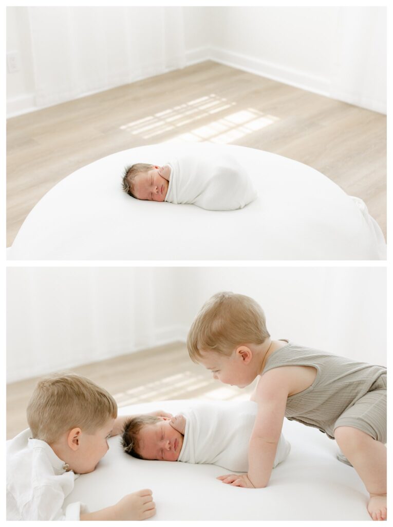 Two toddler brothers in white and tan neutral outfits sitting next to their newborn baby brother wrapped in a white blanket during a Charleston newborn session prep.