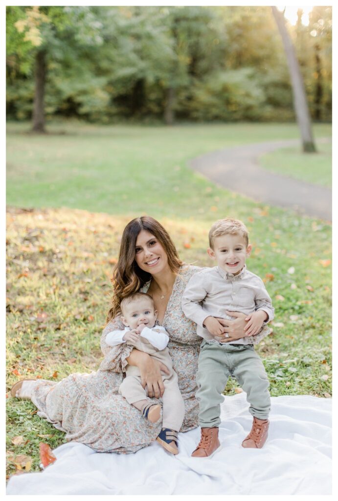 Fall family portraits in Charleston with mom holding infant boy and toddler boy, framed by vibrant fall foliage.