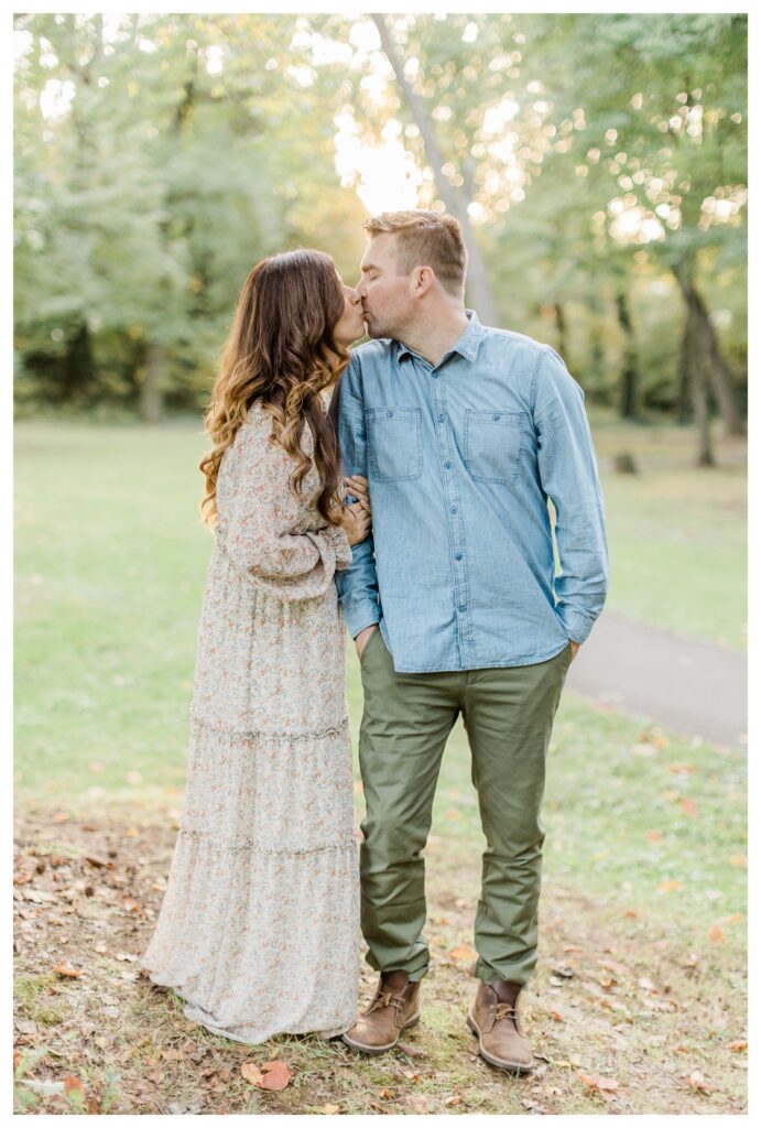 Romantic fall family portraits in Charleston with mom and dad sharing a kiss under vibrant fall leaves, capturing a tender moment amidst the autumn scenery